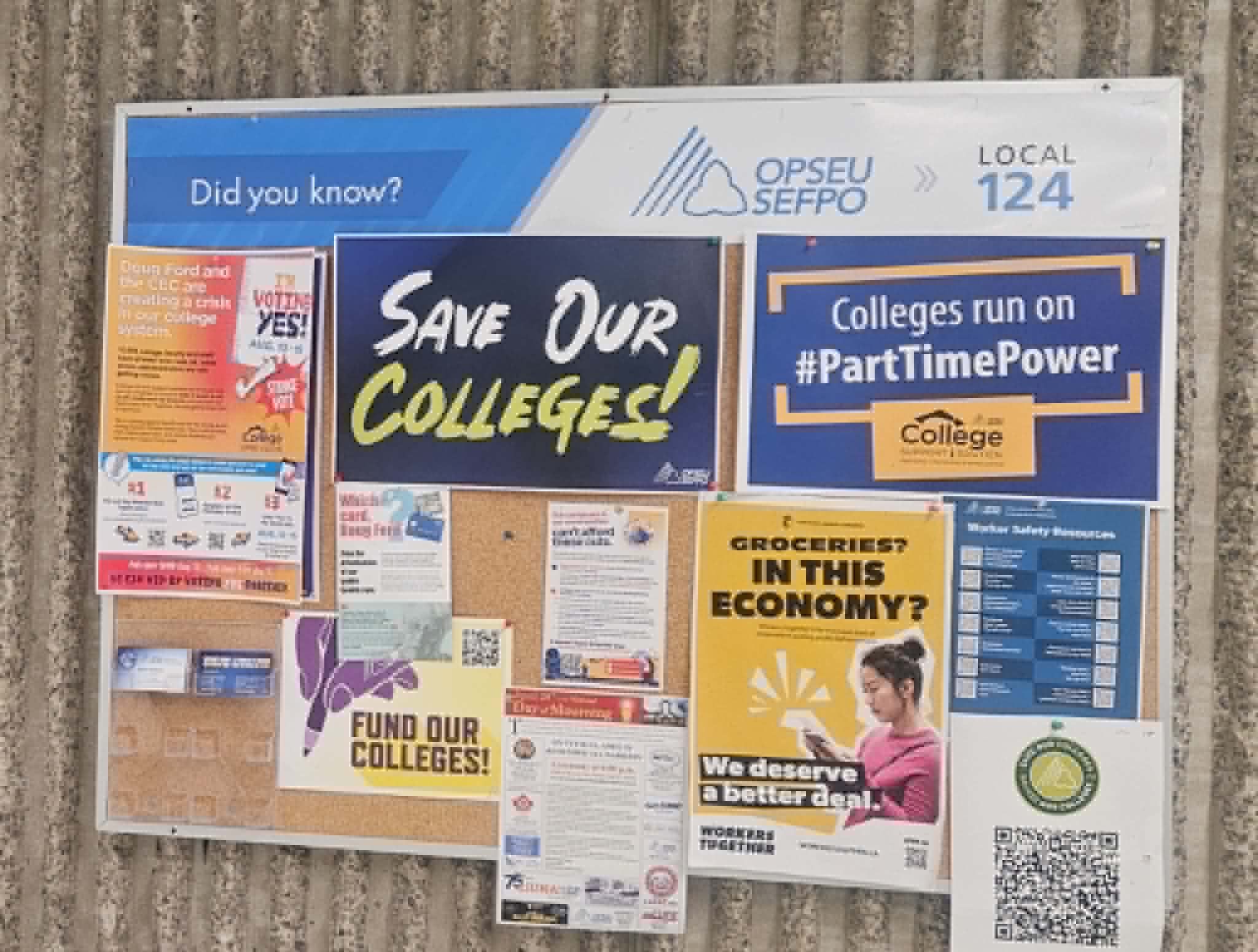 Photograph of a densely posted union bulletin board with campaign posters, QR codes, and contact cards
